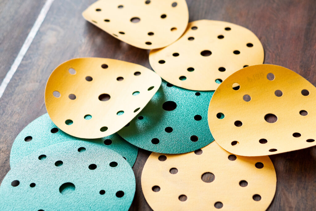 Bois brun texturé en fond. Huit disques abrasifs de qualité de différentes granularités pour le ponçage manuel.