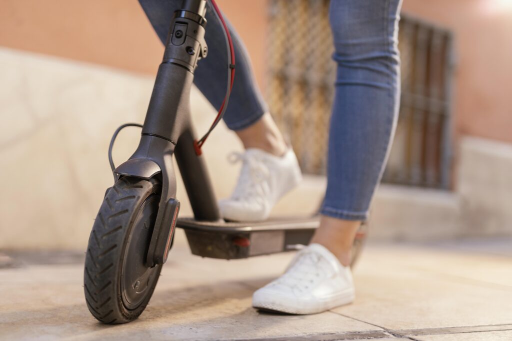 Une jeune femme monte sur sa trottinette électrique noire en ville.